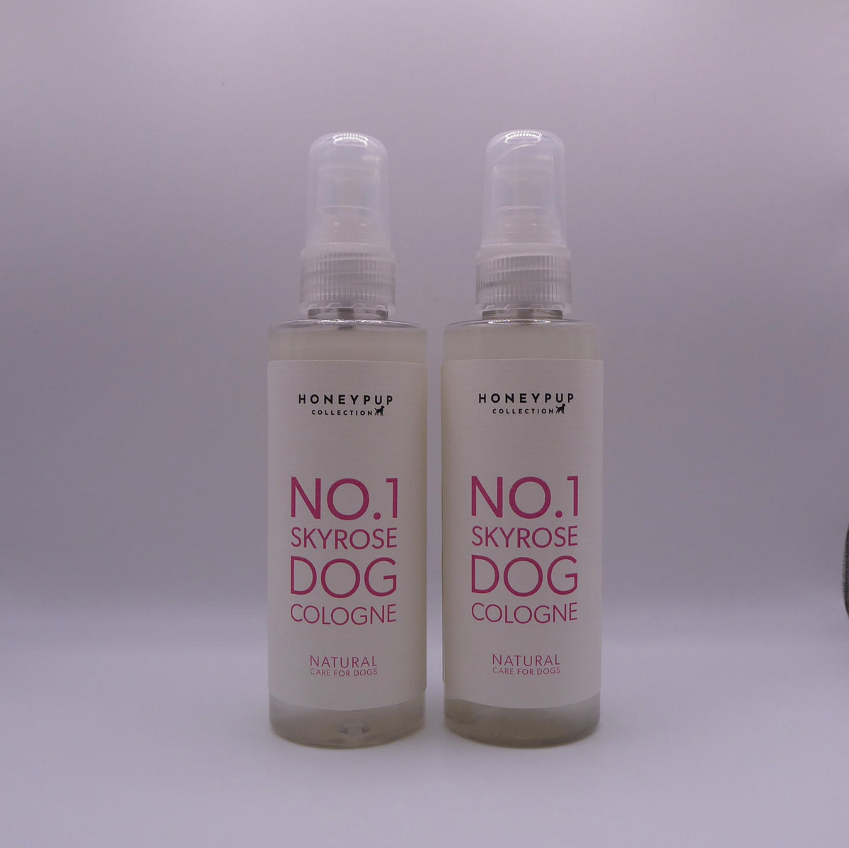 Two clear plastic spray bottles of Honeypup Collections No.1 Skyrose Dog Cologne with white labels and pink text, set against a plain light gray background.